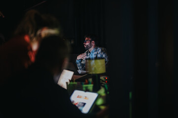 A group of business coworkers are engaged in a late-night project in a dimly lit office setting,...