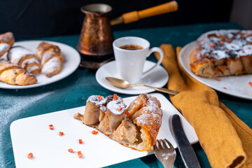 Banana dessert Tarte tatin and croissants on a dark green background with a cup of coffee brewed in a cezve and freeze-dried raspberries.