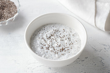 Healthy Chia Seed Pudding in White Bowl with Spoon and Dry Chia Seeds on Light Background