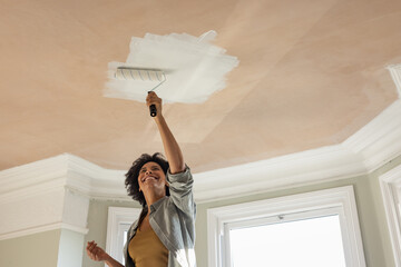 Happy Woman Applying Paint to Ceiling with Roller