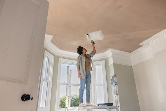 Woman Painting Ceiling with Roller in a large room