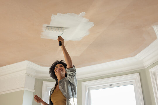 Happy Woman Applying Paint to Ceiling with Roller