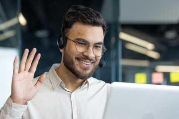 Fototapeta premium Man with headset and laptop inside office. Online customer support worker talking using video call. Businessman close up on business meeting conference with colleagues.