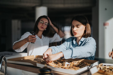 Two business employees take a break from work to share a pizza in a modern office, creating a relaxed and friendly atmosphere.