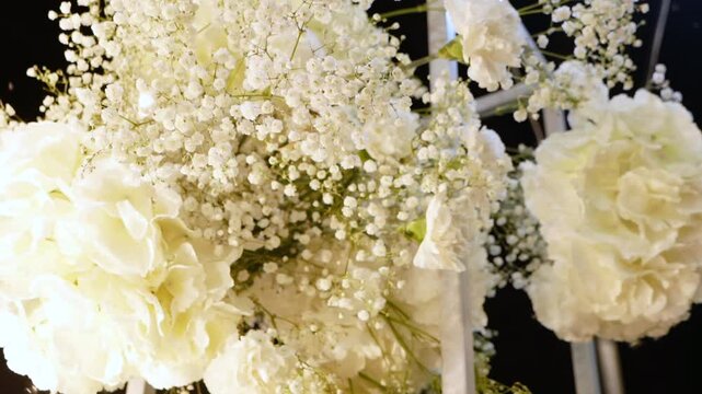 Evening wedding arch of white flowers and greenery with lanterns outdoors. Floristry and decor at the solemn ceremony. Large white cake with cream