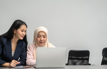 Professional business discussion between two female colleagues using laptop in modern office,...