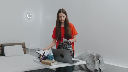 Teenager organizes school supplies in backpack while studying at a bright, modern bedroom desk in the afternoon light