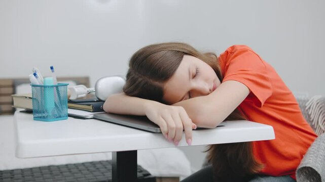 teenage girl feels exhausted while studying at a desk in a modern bedroom during the day, overwhelmed by schoolwork and fatigue