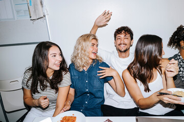 Happy young man spending leisure time with female roommates sitting in college dorm room