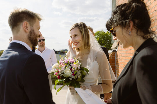 Loving couple looking at each other while standing near female minister during wedding ceremony