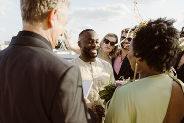 Happy groom standing with bride amidst guests while exchanging vows at ceremony
