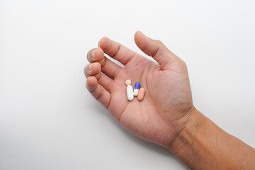 A close-up image showing an open hand holding several elongated pills the background is uniformly light gray, emphasizing the simplicity and focus on the subject