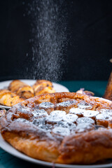Banana Tarte Tatin is sprinkled with powdered sugar on a white plate on a dark background. The powder is poured onto the cake. Vertical Photo