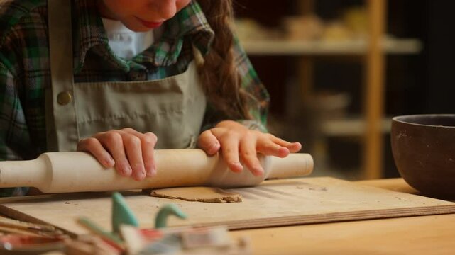 Close up Caucasian teen little girl daughter child kid schoolgirl artist potter using wooden rolling pin shaping porcelain clay material making craft shape pottery art ceramics indoor workshop studio