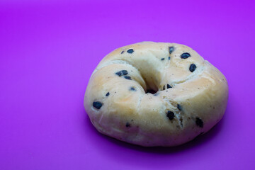 A close-up photo of a blueberry bagel, showing its chewy texture and juicy blueberries. contrasts with the purple background. Perfect for a break.