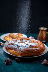 Banana Tarte Tatin is sprinkled with powdered sugar on a white plate on a dark background. The powder is poured onto the cake. Vertical Photo