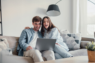 Happy emotional positive young family couple woman man looking at computer screen, celebrating...