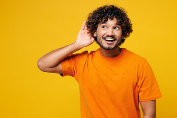 Young curious nosy happy Indian man he wear orange t-shirt casual clothes try to hear you overhear...