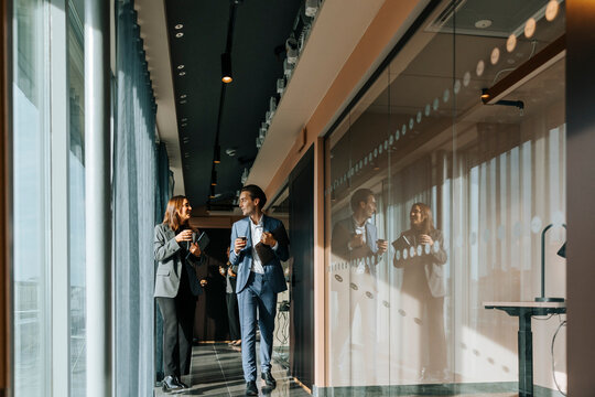 Male and female business professionals talking while walking at office corridor