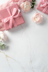 Pink gift boxes with ribbons and delicate ranunculus flowers on a marble background. Perfect for celebrations, weddings, or romantic occasions.