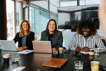 Happy multiracial female business professionals sitting in board room at office