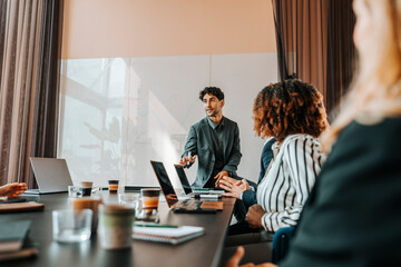 Young male entrepreneur brainstorming colleagues sitting in board room at office