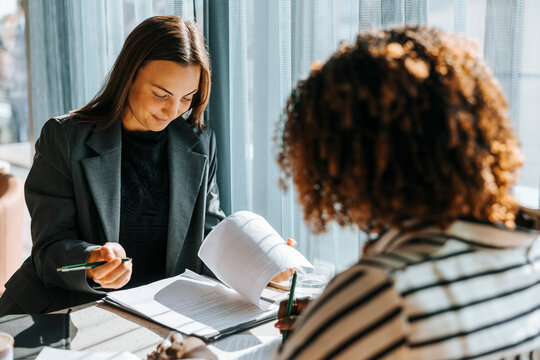 Female business professional reviewing contract while sitting with client at office