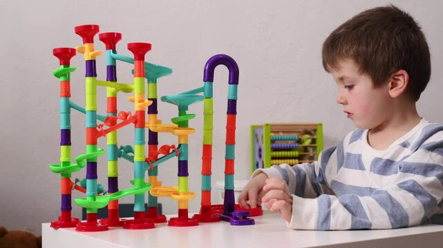 A 5-year-old boy plays with a multi-colored construction set, a labyrinth for balls. Development of logic and fine motor skills in preschool children. Independent play