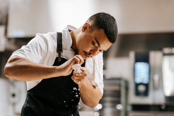 Young male chef wearing apron grating cheese for garnishing in kitchen