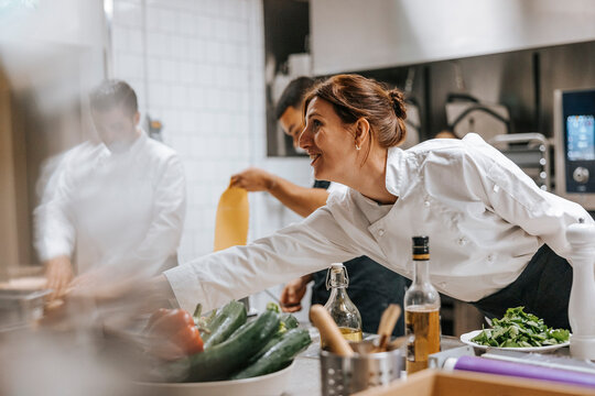 Happy female chef reaching for food at kitchen counter in restaurant