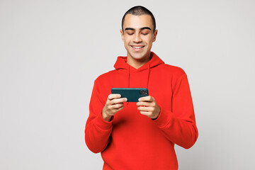 Young middle eastern man he wear red hoody casual clothes use play racing app on mobile cell phone hold gadget smartphone for pc video games isolated on plain solid white background Lifestyle concept © ViDi Studio