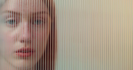 A red-haired woman with freckles looks at the camera with a serious look standing behind striped...