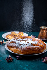 Banana Tarte Tatin is sprinkled with powdered sugar on a white plate on a dark background. The powder is poured onto the cake. Vertical Photo