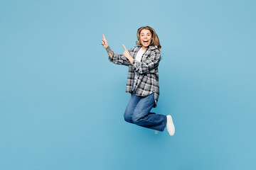 Obraz premium Full body sideways young woman she wears checkered grey shirt casual clothes jump high point index finger aside on area mock up isolated on plain pastel light blue cyan background. Lifestyle concept.