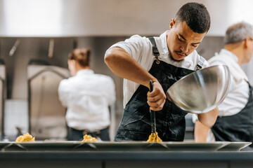 Focused young male chef plating pasta in plate at commercial kitchen
