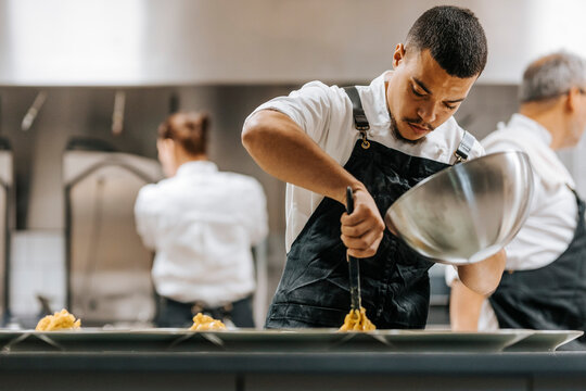 Focused young male chef plating pasta in plate at commercial kitchen