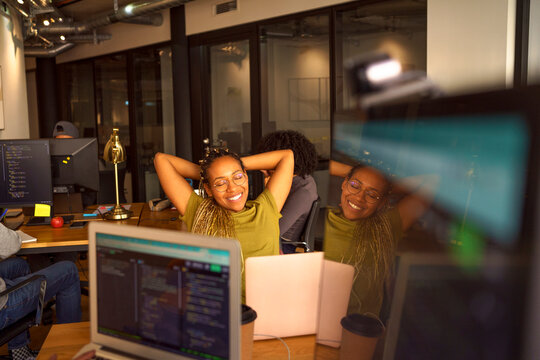 Smiling female programmer relaxing with hand behind head in office