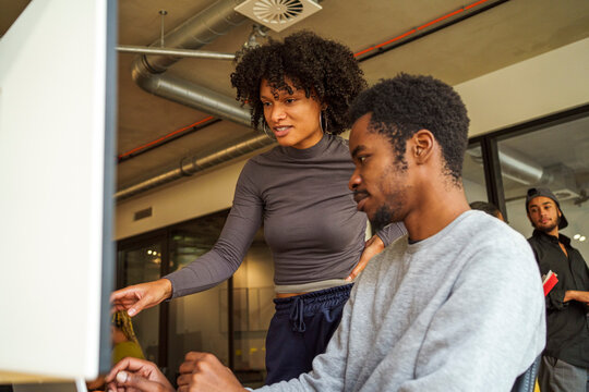 Low angle view of young coding professional talking with male colleague working on desktop PC in office