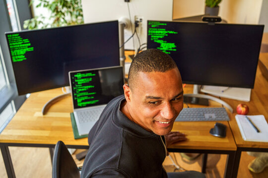 High angle view of smiling male IT professional sitting near desktop PC in office