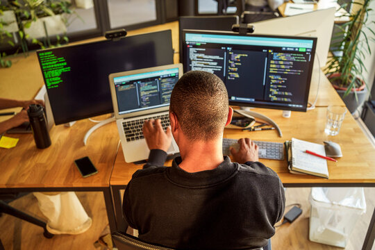 High angle rear view of male computer programmer sitting near desk in office
