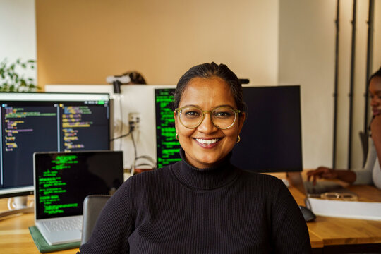Portrait of happy businesswoman near desktop PC in tech startup office