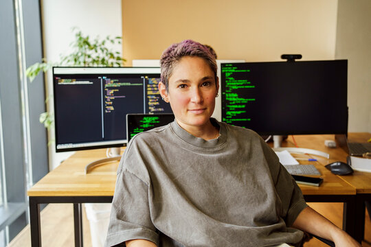 Portrait of non-binary computer programmer sitting in front of desktop PC at office
