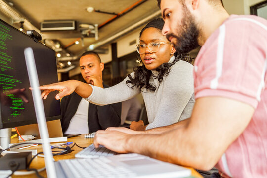 Female computer programmer pointing at desktop screen while discussing with male coworker in office