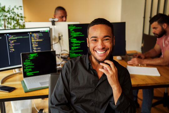 Portrait of happy male businessman sitting in front of desktop PC in office