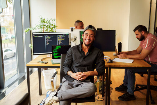 Portrait of happy male IT professional sitting in front of desktop PC in office