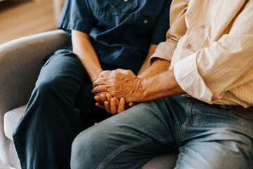 Midsection of senior male holding hands of female caregiver while sitting on sofa at nursing home