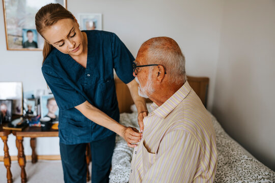 Female caretaker assisting senior man wearing shirt at nursing home