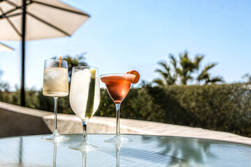 A variety of cocktails in different types of glasses on a glass-topped table. Midday happy hour time in tropical climate. Resort, holiday refreshment concept.
