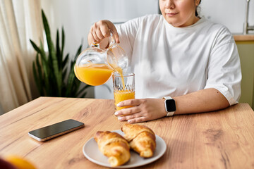 A young woman enjoys a delightful breakfast, pouring orange juice while sitting at a cozy table.