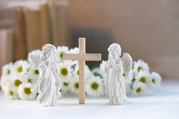 Beautiful angel figurines with wooden cross and flowers on table close up. symbol of Christianity religion, faith in God, prayer, memory. christian home altar
